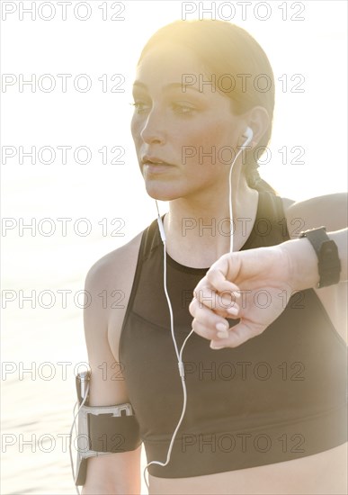 Woman wearing headphones checking wrist watch on beach