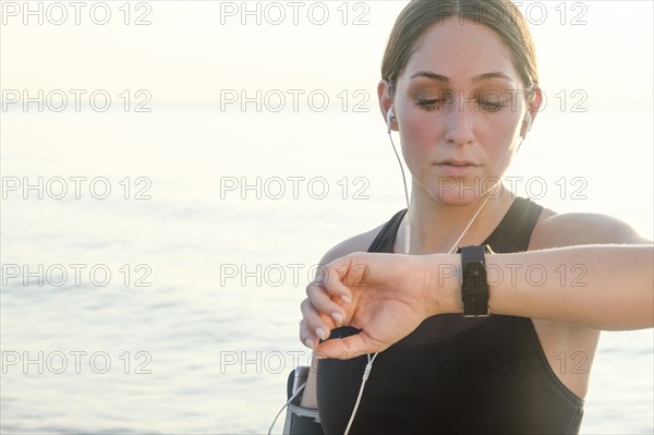 Woman wearing headphones checking wrist watch on beach