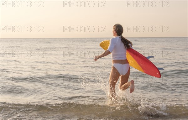 Woman holding surfboard running into sea