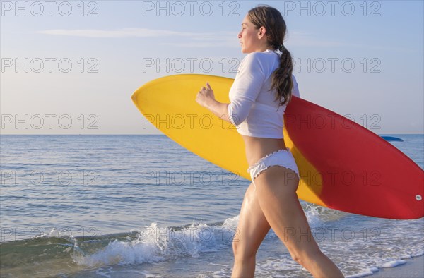 Woman holding surfboard running into sea