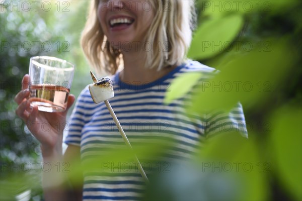 Smiling woman holding glass of wine and toasted marshmallow