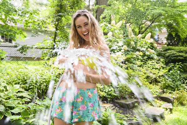 Smiling young woman holding garden hose