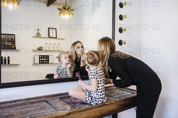 Mother and daughter applying lipstick in mirror