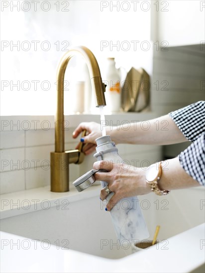 Hands of woman filling water bottle in kitchen sink