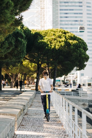 Young man using electric scooter on pavement