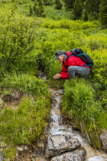 Senior man drinking from stream