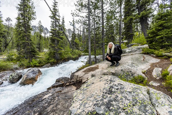 Mature woman crouching on rocks by river in Stanley