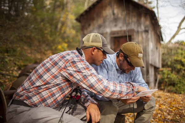 Men holding fishing rods and box by log cabin