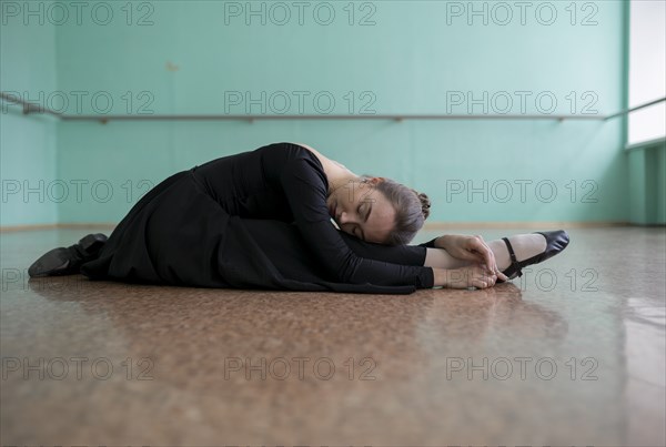 Ballet dancer wearing black dress stretching in studio