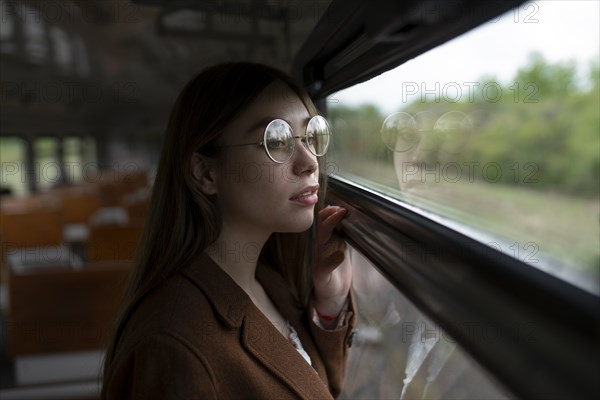 Young woman wearing glasses looking out of train window