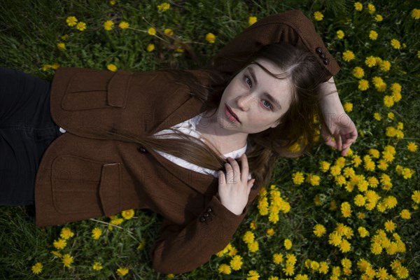 Young woman wearing brown blazer lying on yellow flowers