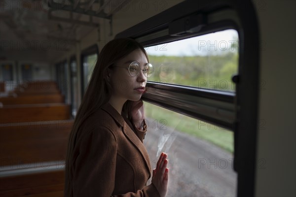 Young woman wearing glasses looking out of train window