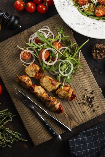 Grilled meat skewers and salad on cutting board