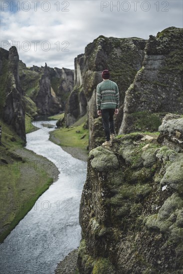 Young man standing on cliff above canyon in Kirkjubµjarklaustur