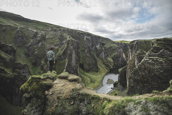 Young man standing on cliff above canyon in Kirkjubµjarklaustur