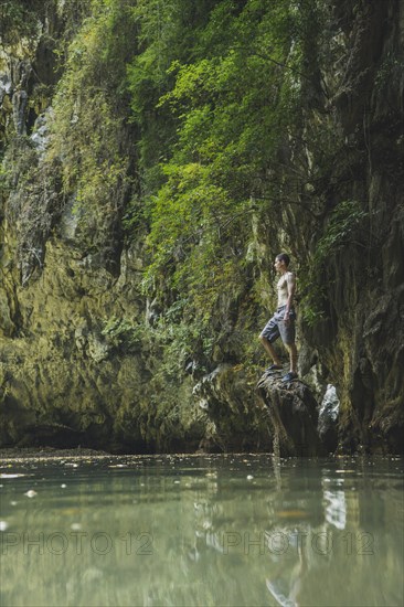 Shirtless man standing on rock in lake by cliffs in Krabi