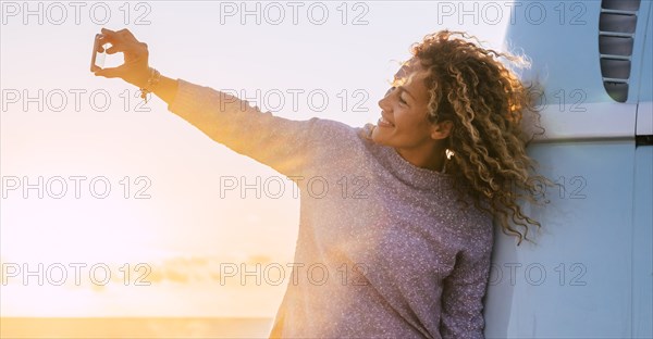 Woman taking selfie by camper van at sunset