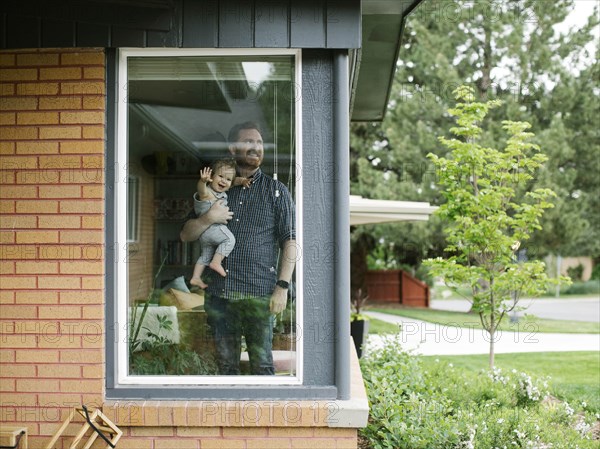 Father holding his daughter behind window of house