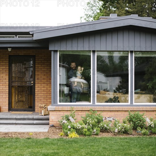 Father holding his daughter behind window of house