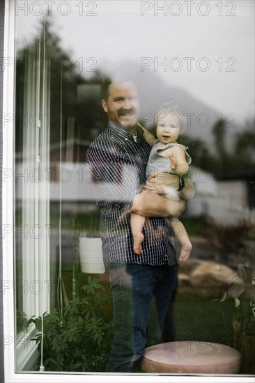 Father holding his daughter behind window