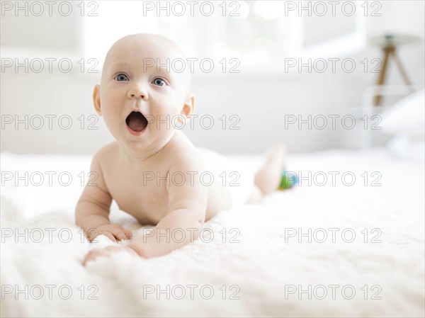 Shirtless baby boy lying on bed with his mouth open