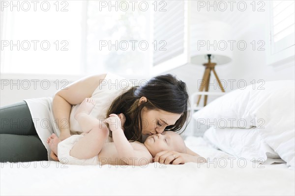 Mother kissing her son's cheek on bed