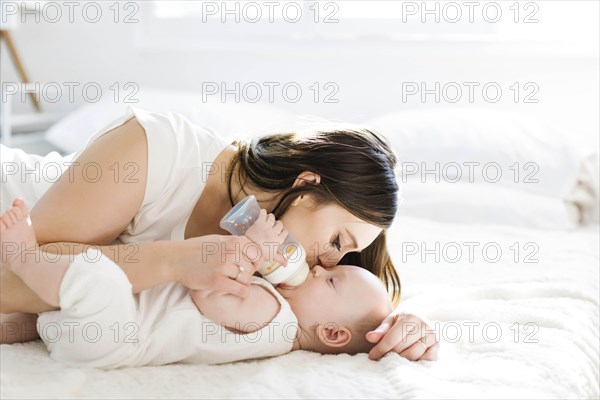 Mother kissing her son's cheek as he drinks bottle of milk