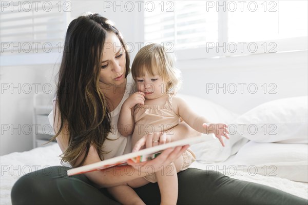 Woman reading book to her daughter on bed
