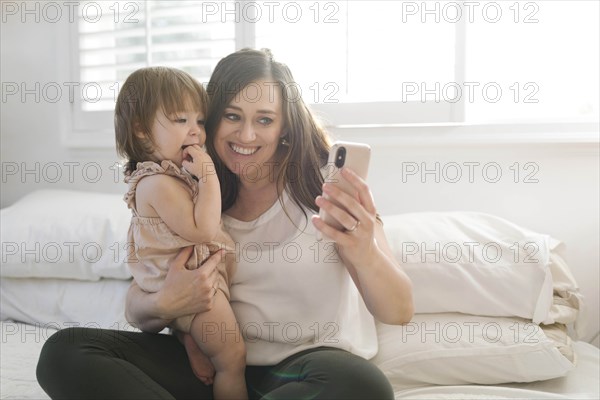 Mother and daughter taking selfie on bed