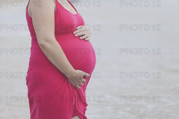 Pregnant woman wearing pink dress on beach