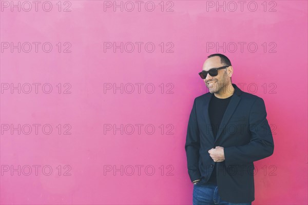 Smiling man wearing sunglasses and blazer by pink wall