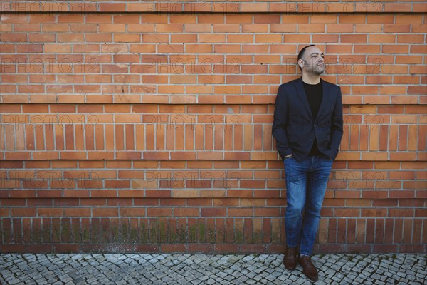 Man wearing blazer and jeans by brick wall