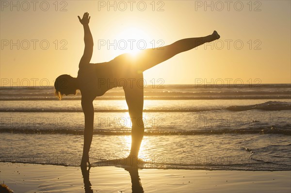 Silhouette of woman doing yoga on beach at sunset