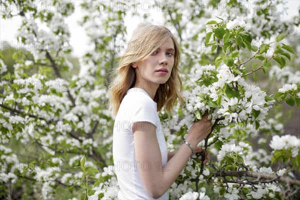 Blond haired young woman among white blossoms