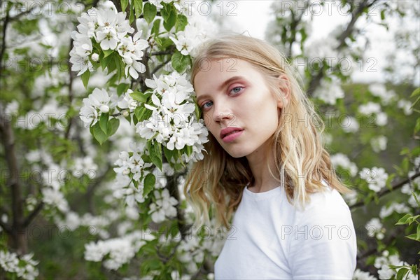 Blond haired young woman among white blossoms