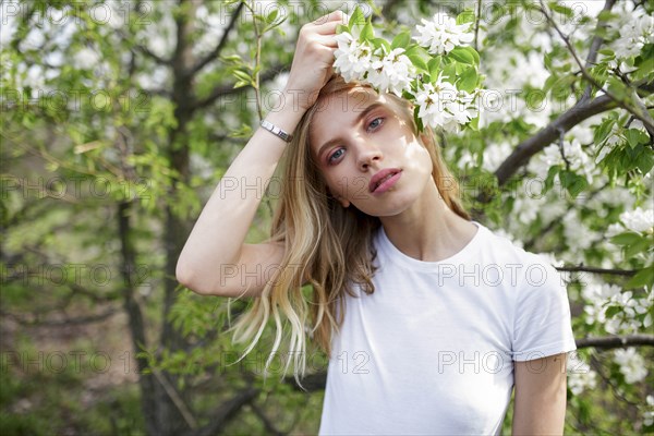 Blond haired young woman among white blossoms