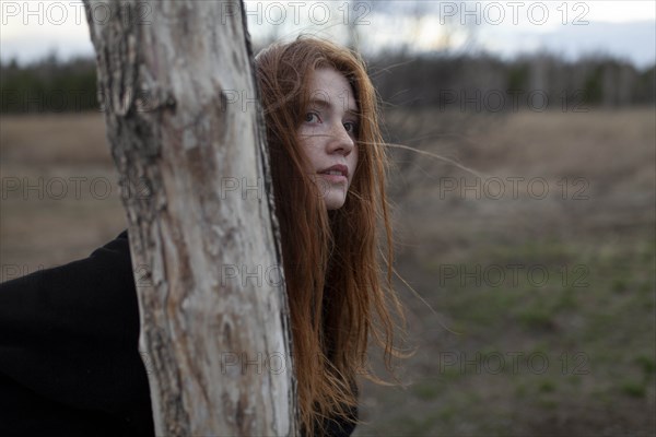 Windswept teenage girl by tree trunk