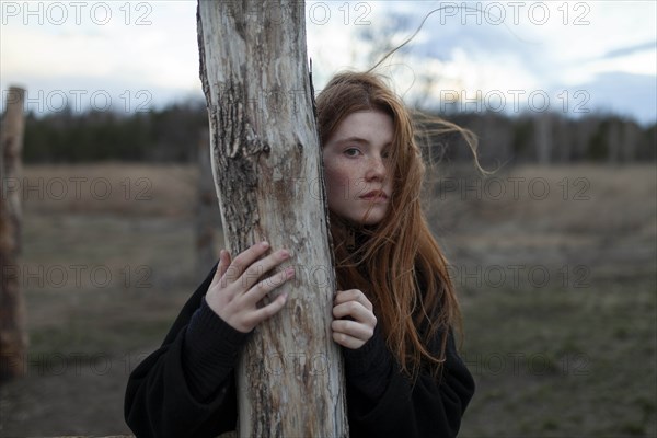 Windswept teenage girl by tree trunk