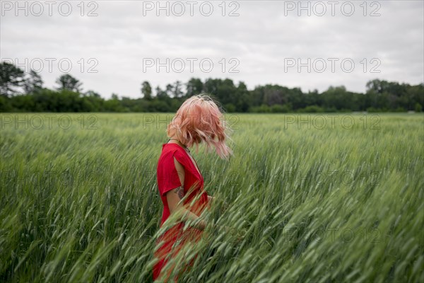 Woman with pink hair wearing red dress in wheat field