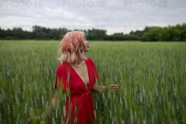 Woman with pink hair wearing red dress in wheat field