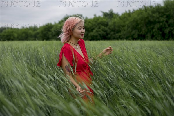 Woman with pink hair wearing red dress in wheat field