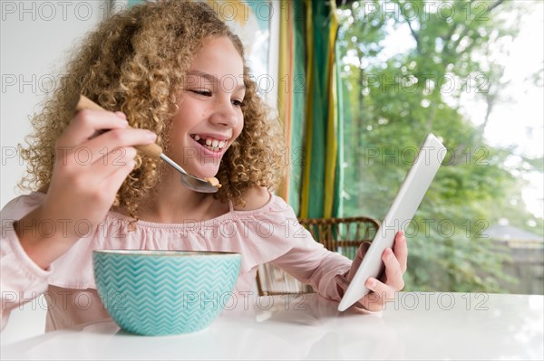 Smiling girl eating breakfast using tablet