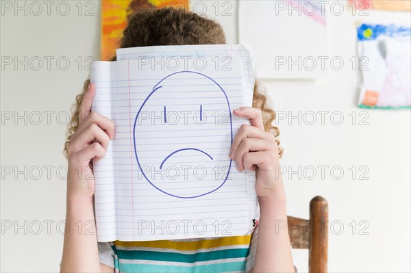 Girl holding note pad with drawing of sad face
