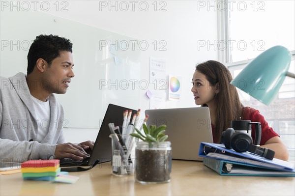 Coworkers using laptops in office