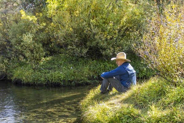 Man sitting on grass by steam in Stanley, Idaho, USA