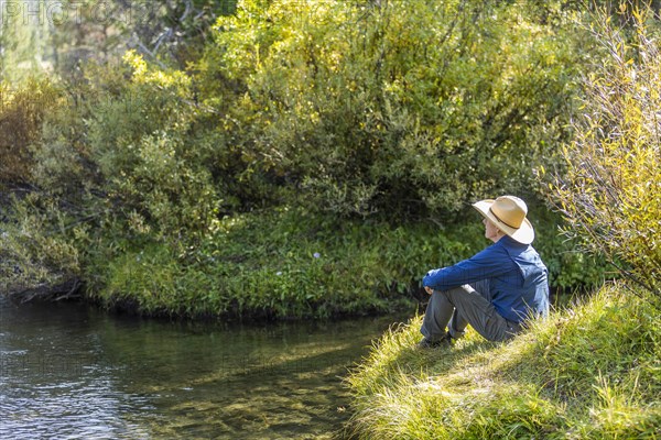 Man sitting on grass by steam in Stanley, Idaho, USA