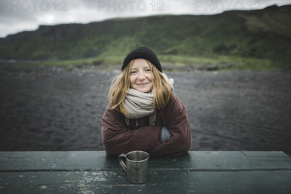 Young woman wearing warm clothing at picnic table on beach