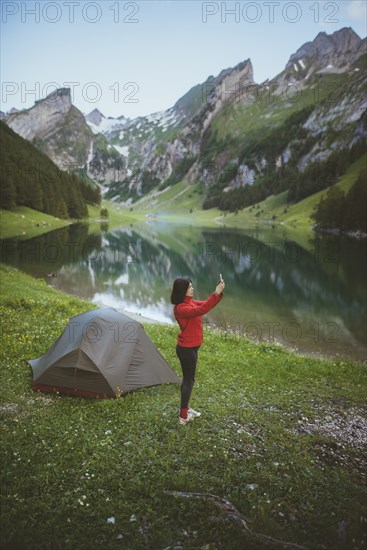 Woman taking photograph by tent near Seealpsee lake in Appenzell Alps, Switzerland