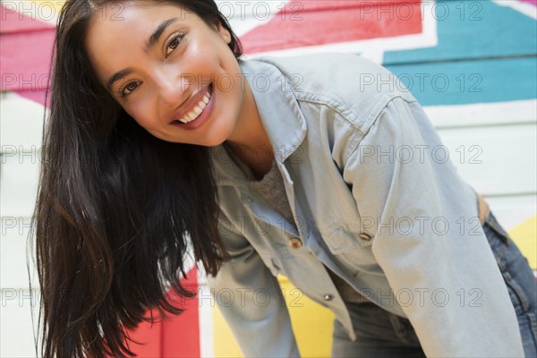 Smiling woman leaning forward against colorful wall