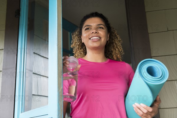 Smiling woman holding drink bottle and yoga mat